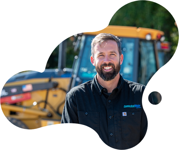 CT Water employee looking at the camera in front of a backhoe